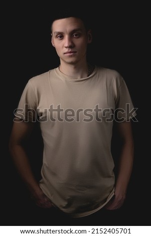 Handsome young man posing over black background. Studio photo with one light source. A serious guy stands with his hands in his pockets.