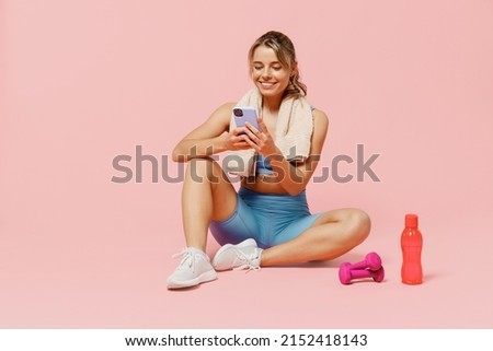 Full size young sporty fitness trainer instructor woman wear blue tracksuit spend time in home gym sit on floor use mobile cell phone isolated on plain light pink background. Workout sport concept. Royalty-Free Stock Photo #2152418143