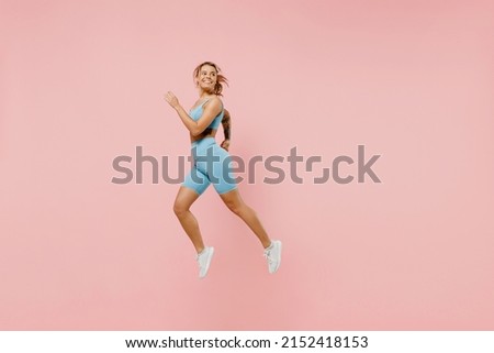 Full size young strong sporty athletic fitness trainer instructor woman wear blue tracksuit spend time in home gym jump high run isolated on pastel plain light pink background. Workout sport concept