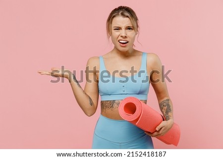 Young sad wondered strong sporty athletic fitness trainer instructor woman wear blue tracksuit spend time in home gym spread hand isolated on pastel plain light pink background. Workout sport concept