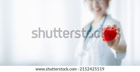 Female doctor standing holding a small red heart, a hospital cardiologist. Modern medical concepts in cardiology and disease treatment. copy space.