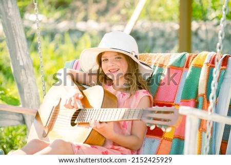 Little child playing guitar. Fashion kid girl. Kids music guitar school. Summer activity for children in warm weather. Cute little girl having fun on a swing in beautiful summer garden.