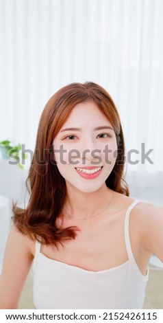 point of view asian brunette shoulder length hair girl take selfie smile look at camera in white room