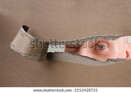 blank cardboard form, craft paper, hole with Human eye, mature man, senior 60 years old looking straight, covertly is following, concept of secrecy, spying, Surveillance System, face Recognition Royalty-Free Stock Photo #2152428731