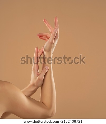 Cropped shot of woman applying cosmetic product on her hands on a beige background. Young woman applying hand cream. Royalty-Free Stock Photo #2152438721