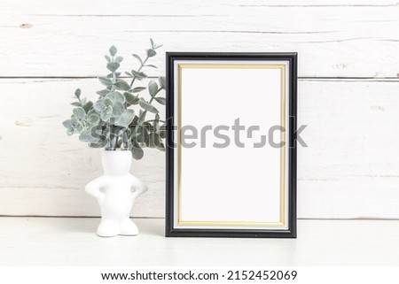 Mockup of a vertical black frame 10x15 cm on a light background. Black vertical frame with flowers on the table.