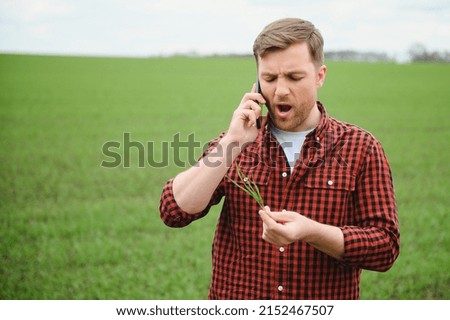 Young handsome farmer walking on farmland, and talking on cell phone.