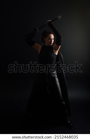 Full length portrait of pretty redhead female model wearing black futuristic scifi leather  costume. Standing pose with dark studio background 