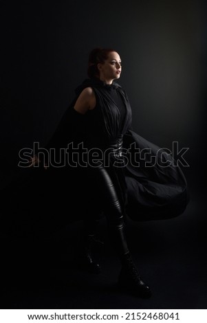 Full length portrait of pretty redhead female model wearing black futuristic scifi leather  costume. Standing pose with dark studio background 