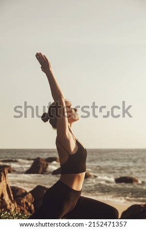Young woman does yoga for healthy lifestyle on sea beach. Female performing sports exercises to restore strength and spirit. Yoga position. Copy space Royalty-Free Stock Photo #2152471357
