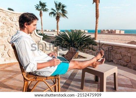 a man with a laptop in his hands is resting and working as a freelancer on the background of palm trees