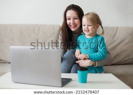 Mother and her daughter using video chat on laptop sitting on cozy sofa at home, watching video, having fun, two generations