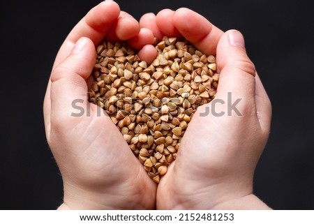Children's hands hold buckwheat. Cereal crops. Dark background.