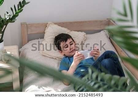 Happy boy watching cartoons on smartphone while lying on bed. A child looks into smartphone. Technology, internet, leisure for children
