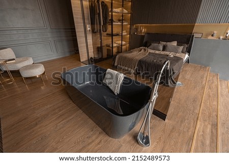 bedroom and freestanding bath behind a glass partition in a chic expensive interior of a luxury home with a dark modern design with wood trim and led light Royalty-Free Stock Photo #2152489573