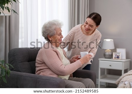 Young caregiver giving tea to senior woman in room. Home care service Royalty-Free Stock Photo #2152489585