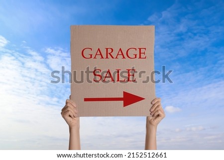 Woman holding sign with text GARAGE SALE against blue sky