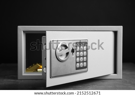 Open steel safe with gold bars on grey table against black background Royalty-Free Stock Photo #2152512671