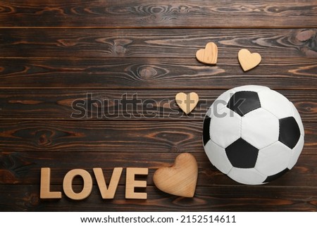 Soccer ball, hearts and word Love on wooden background, flat lay. Space for text