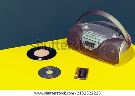 Colorful image of vintage radio player on bright yellow tablecloth isolated over dark green background. Music disks and cassette. Concept of retro pop art, vintage things, mix old and modernity