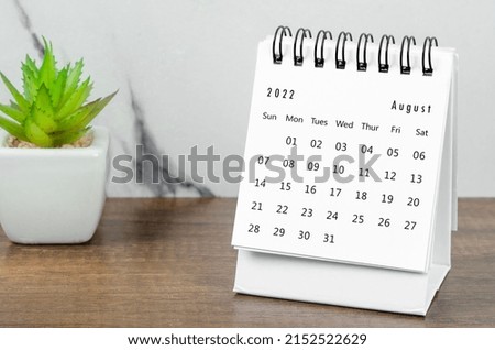 The August 2022 desk calendar with plant pot on wooden table.