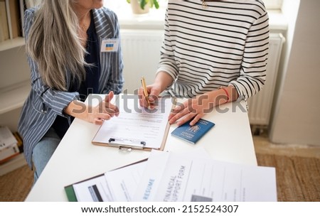 Senior woman volunteer helping Ukrainian woman to fill in forms at asylum centre. Royalty-Free Stock Photo #2152524307