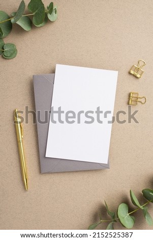 Business concept. Top view vertical photo of paper card grey envelope gold pen binder clips and eucalyptus on beige background with blank space