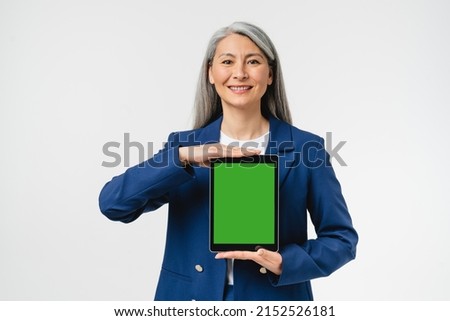 Smiling mature middle-aged businesswoman CEO freelancer in formal attire showing digital tablet with mockup green screen for copy space free space isolated in white background. Sale discount offer