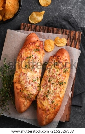 Baguette boats. Hot baked sandwich on baguette bread with ham, bacon, vegetables and cheese on parchment and black dark concrete background. Top view. Copy space.