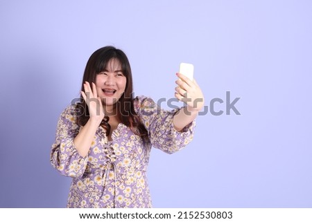 The chubby Asian woman standing on the purple background with the casual clothes.