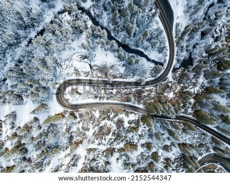 An aerial drone shot of cars on the roads with snowy trees around on a winter day