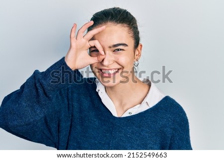 Young caucasian girl wearing casual clothes doing ok gesture with hand smiling, eye looking through fingers with happy face. 