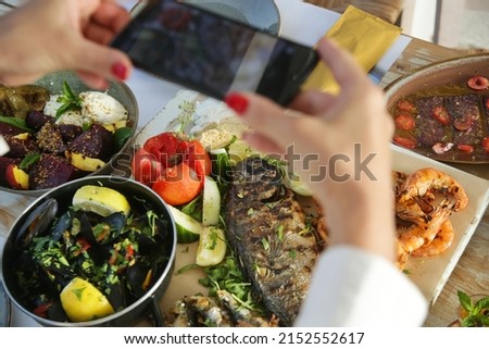 Woman using smartphone to take photos of food before eating in restaurant	
