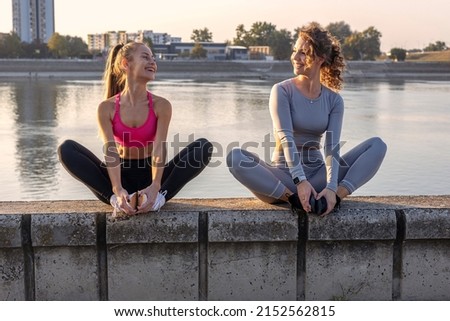 Two woman exercise and stretching outside near the river