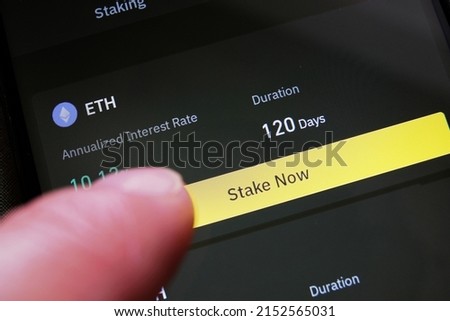 A cryptocurrency investor about to stake Ethereum on a crypto exchange mobile phone app to earn high interest rate. ETH hodler pressing a button to start earning cryptos by staking his holdings. Royalty-Free Stock Photo #2152565031