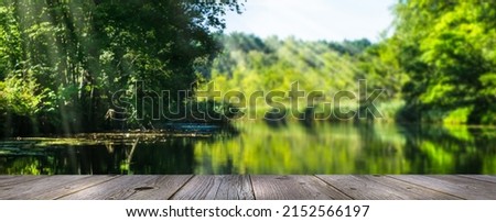 beautiful idyllic forest lake landscape in sunshine, empty wooden planks for advertising display in front of green idyllic blurred water nature, natural concept panorama with copy space Royalty-Free Stock Photo #2152566197