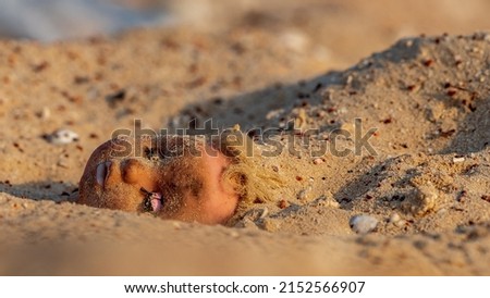 A littered doll head on a sandy beach 
