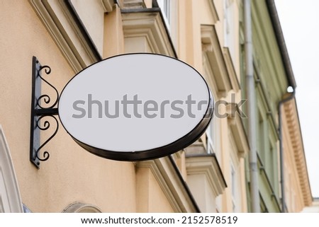 Blank metal oval store signboard on street hanging mounted on the wall. Empty plastic sign board mockup.