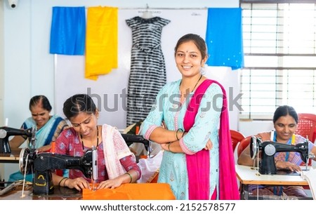 Smiling women standing with crossed arms in front of workers by looking at camera at garments - concept of confident, successful workers and small business. Royalty-Free Stock Photo #2152578577