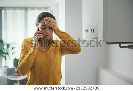Worried woman calling a boiler breakdown emergency service using her smartphone Royalty-Free Stock Photo #2152582705