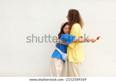 happy woman in basic yellow t-shirt is having fun with child girl 10-11 years old in blue t-shirt. Mom of little kid daughter isolated on white background. Mothers Day love family