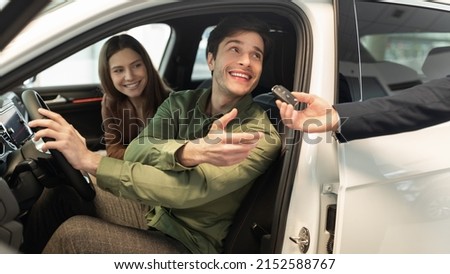 Happy millennial couple taking car key from auto salesman, sitting inside modern automobile at dealership, panorama. Cheery young family buying new vehicle at modern showroom Royalty-Free Stock Photo #2152588767