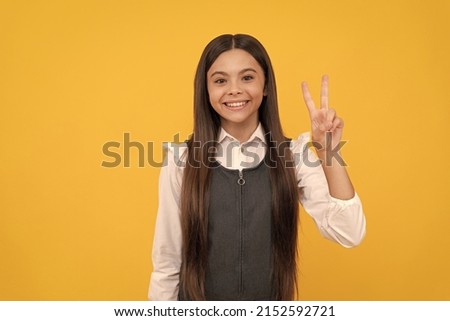 Happy girl child smile showing V sign hand gesture yellow background, peace