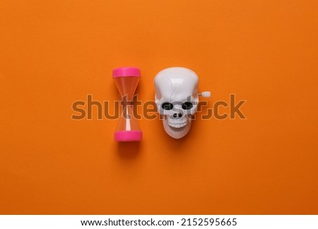 Clockwork skeleton skull toy with hourglass on orange background. Minimal halloween layout. Top view. flat lay