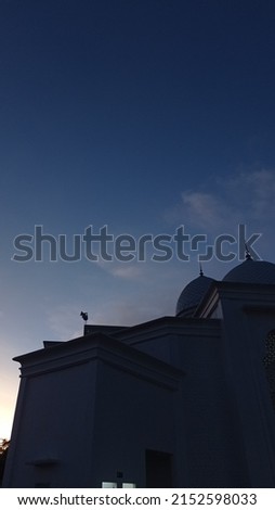 One afternoon at sunset.  the sun sets behind a mosque so that it forms a silhouette in the sky.  the sky is the color of twilight
