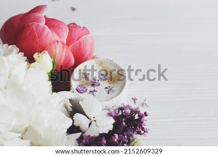 Beautiful peony, lilac, roses flowers arrangement with stylish cup of coffee. Happy mothers day. Good morning. Delicious coffee with lilac petals and stylish bouquet on white wooden background