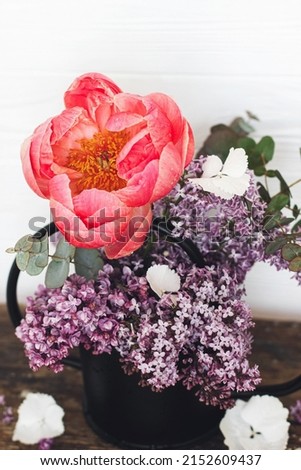 Beautiful peony, lilac  flowers and eucalyptus in stylish metal watering can arrangement on rustic background. Happy mothers day or Valentines day. Hello spring. Modern flowers still life