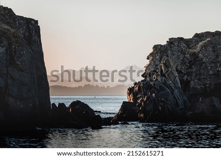 The stone cliffs over the calm sea water with mountains in the background at sunset