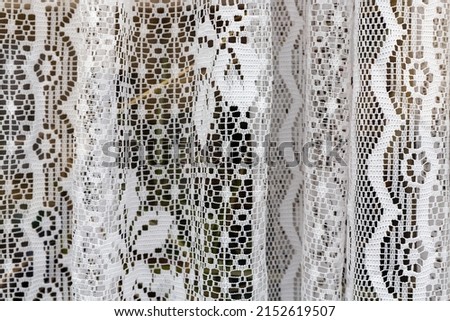 Close up detail of delicate white net curtains seen through a window
