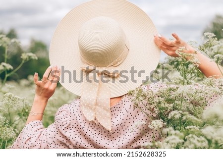 A slender young woman in a pink dress and a straw hat walking in summer meadow among wildflowers,rear view.Summer,beauty,slow life concept. Royalty-Free Stock Photo #2152628325